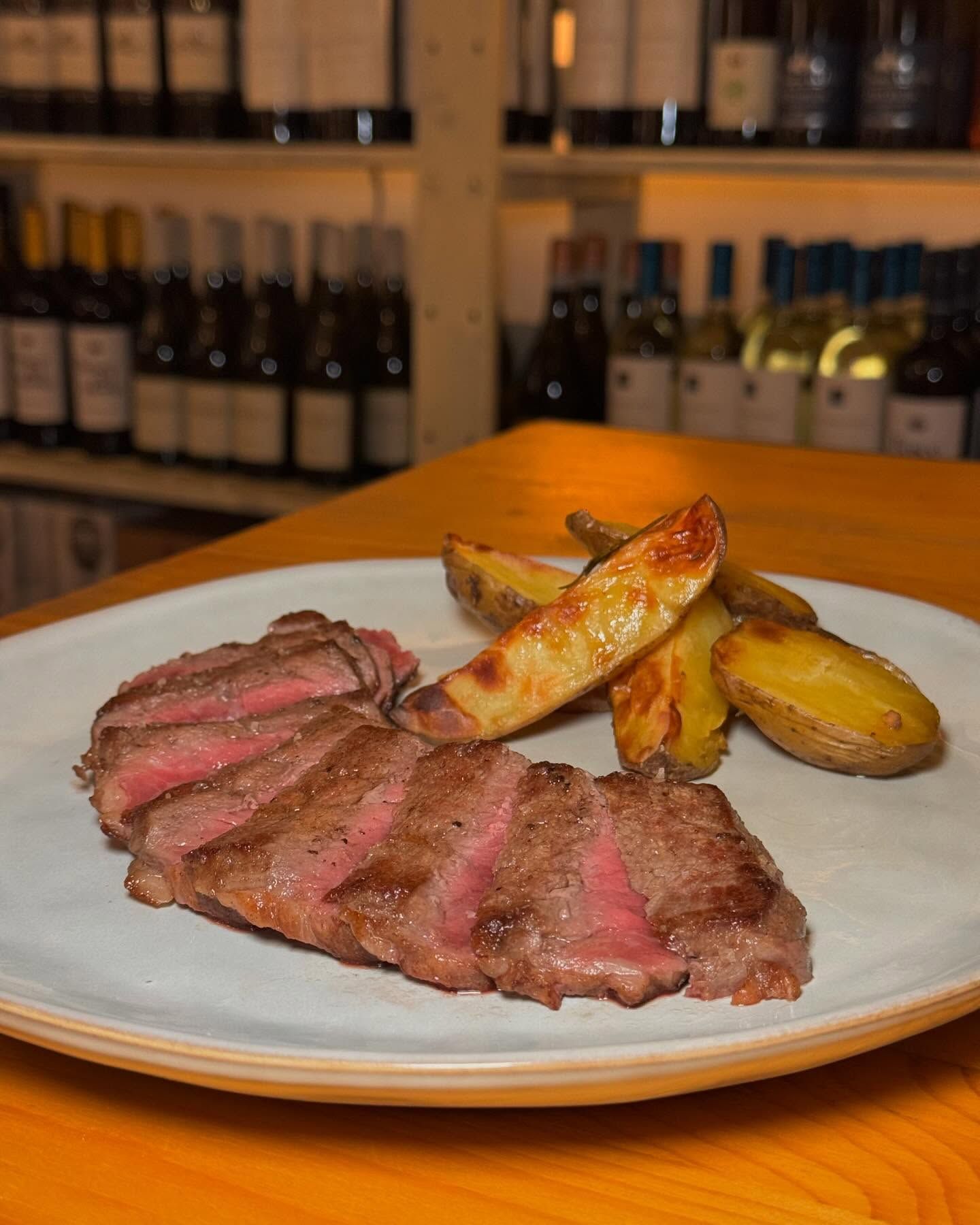Un piatto bianco con sopra una bistecca e spicchi di patate su un tavolo di legno.