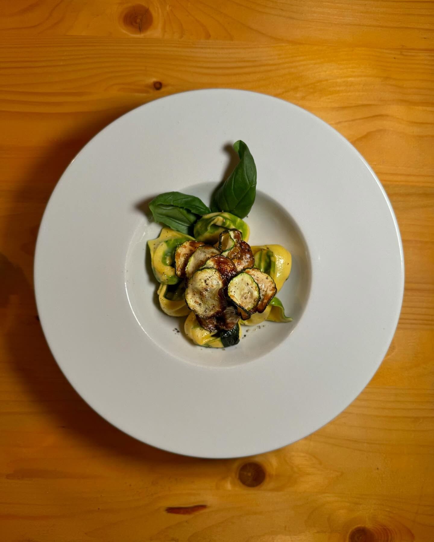 Un piatto bianco con verdure e basilico su un tavolo di legno.