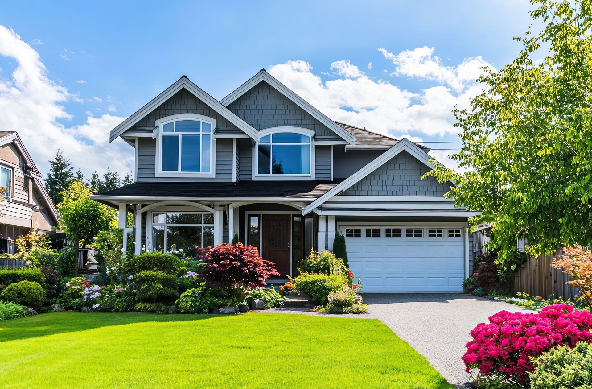 Suburban house with gray siding, white trim, a two-car garage, and a lush green lawn with pink flowers