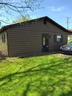 Brown single-story house with a black door, windows, and a parked car on a grassy lawn.