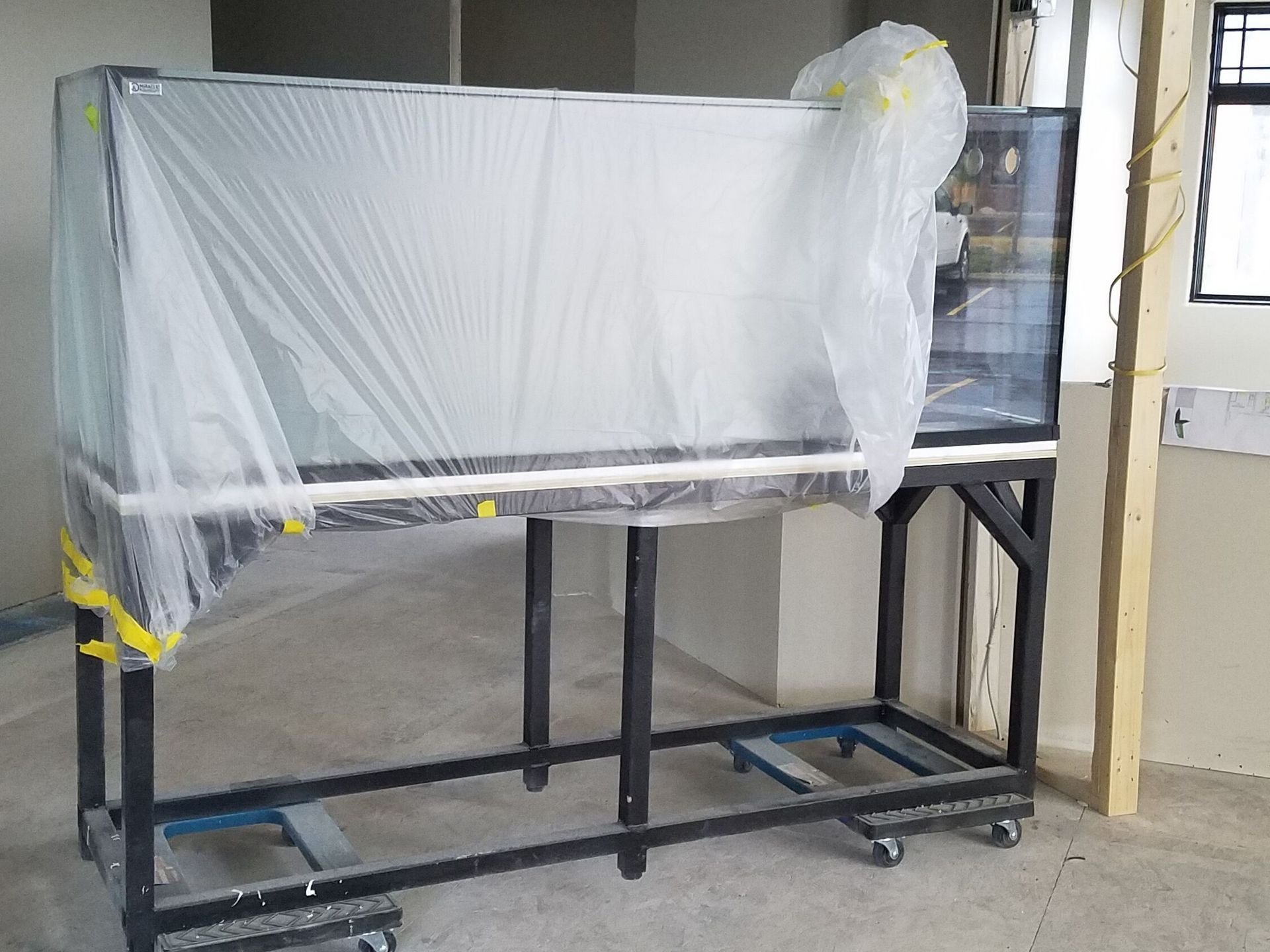 A large aquarium is wrapped in plastic and sitting on a cart.