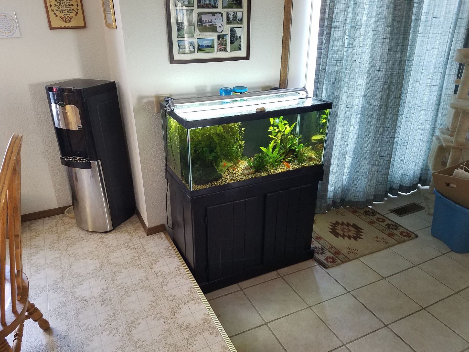 A large fish tank is sitting in a living room next to a water dispenser.