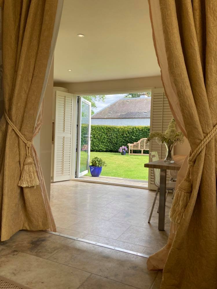 Open window with curtains tied up alongside and view of the garden