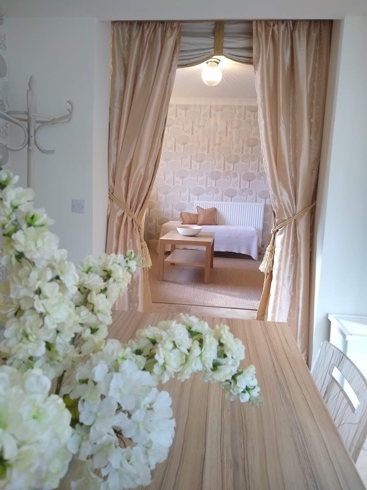 Open curtained doorway into lounge area with ottoman and coffee table - flowers in foreground