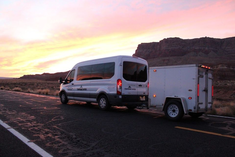 A white van is towing a trailer down a road.