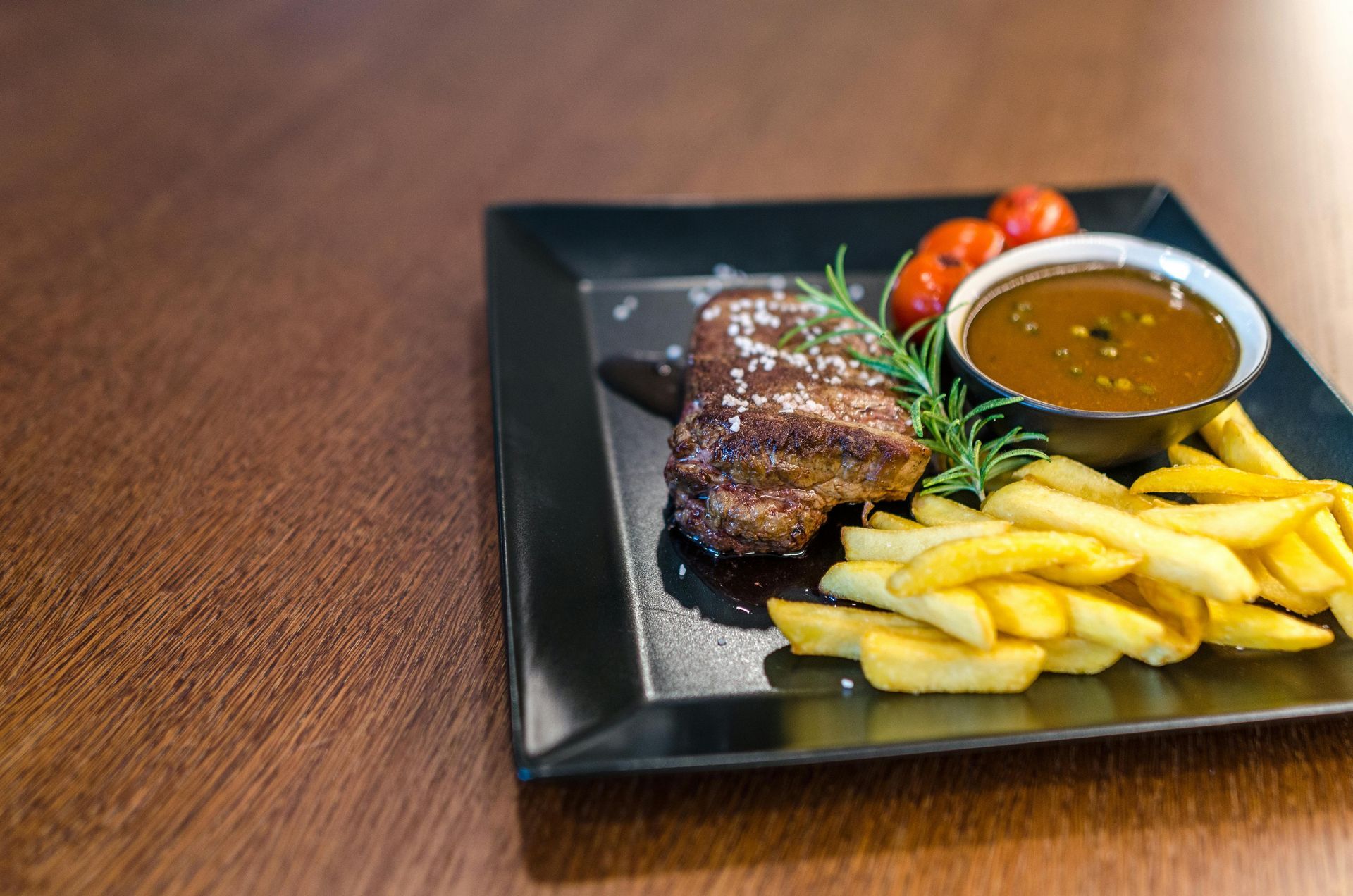 A plate of food with steak and french fries on a wooden table.