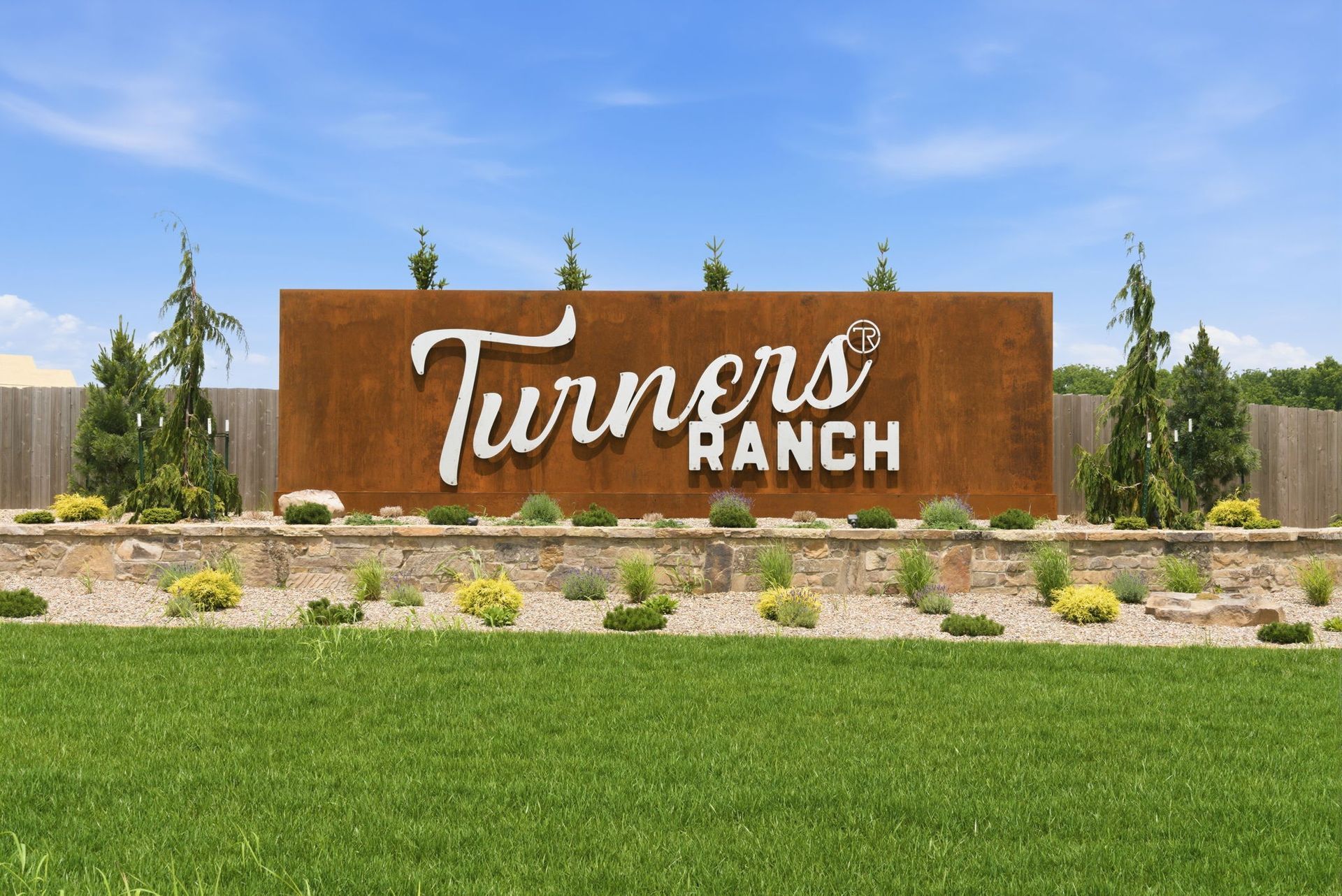 Turners Ranch sign on a brick wall beside a rural field and trees