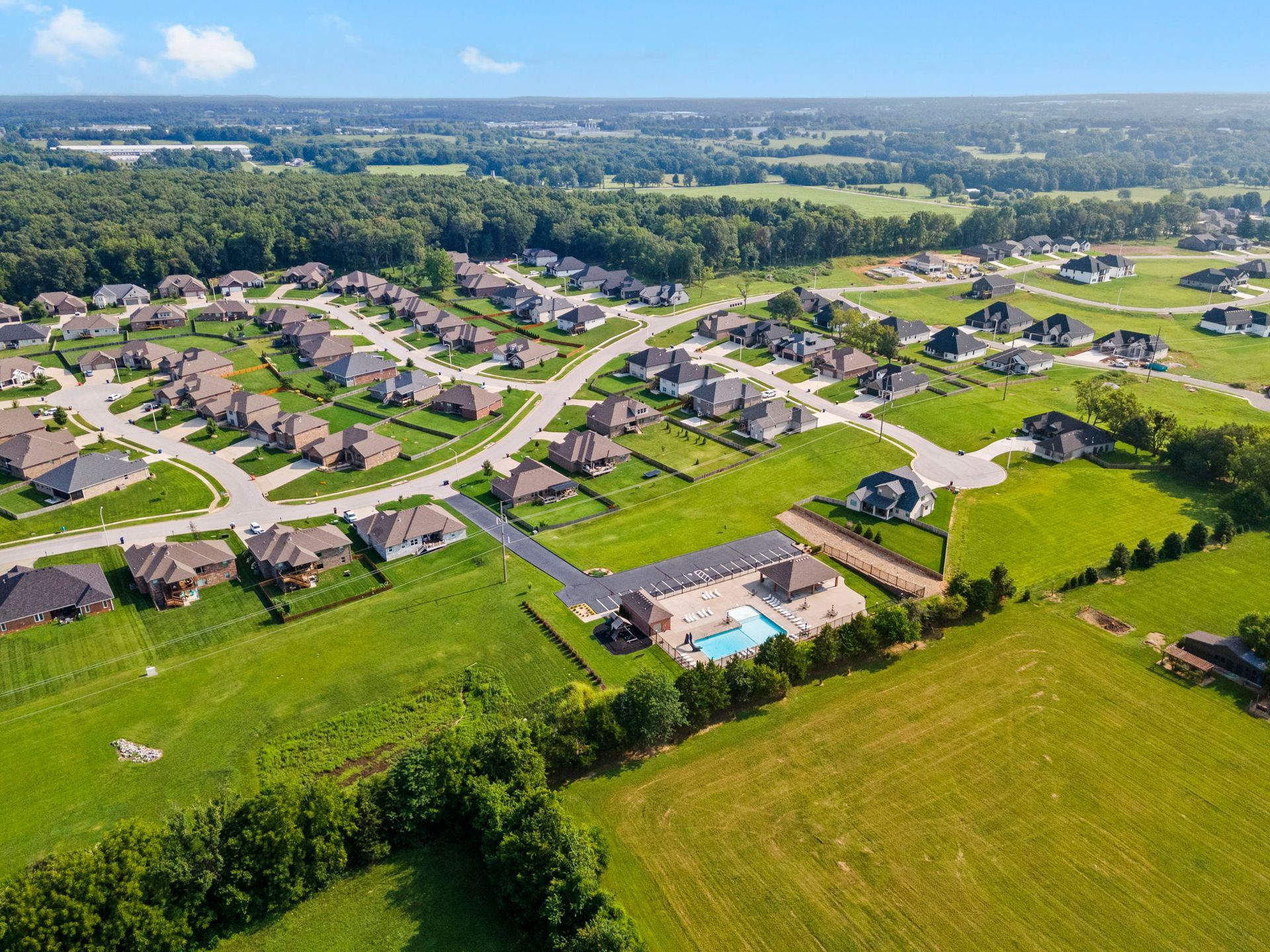 Aerial view of a suburban neighborhood with houses, roads, and a swimming pool on a sunny day.