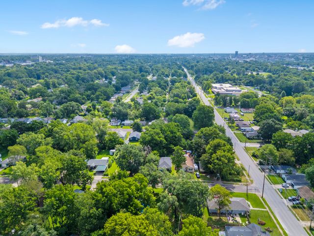 Aerial view of a leafy suburban neighborhood with tree-lined streets and scattered houses under a blue sky