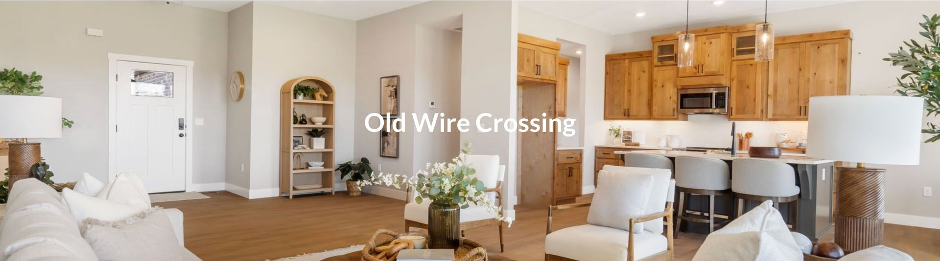 Living room with a white front door, light-colored wood floors, and a kitchen with wooden cabinets.