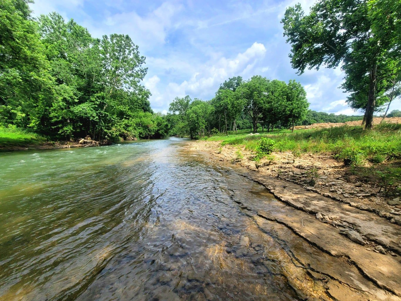 Tan house with brick accents, black shutters, and a two-car garage under a blue sky.
