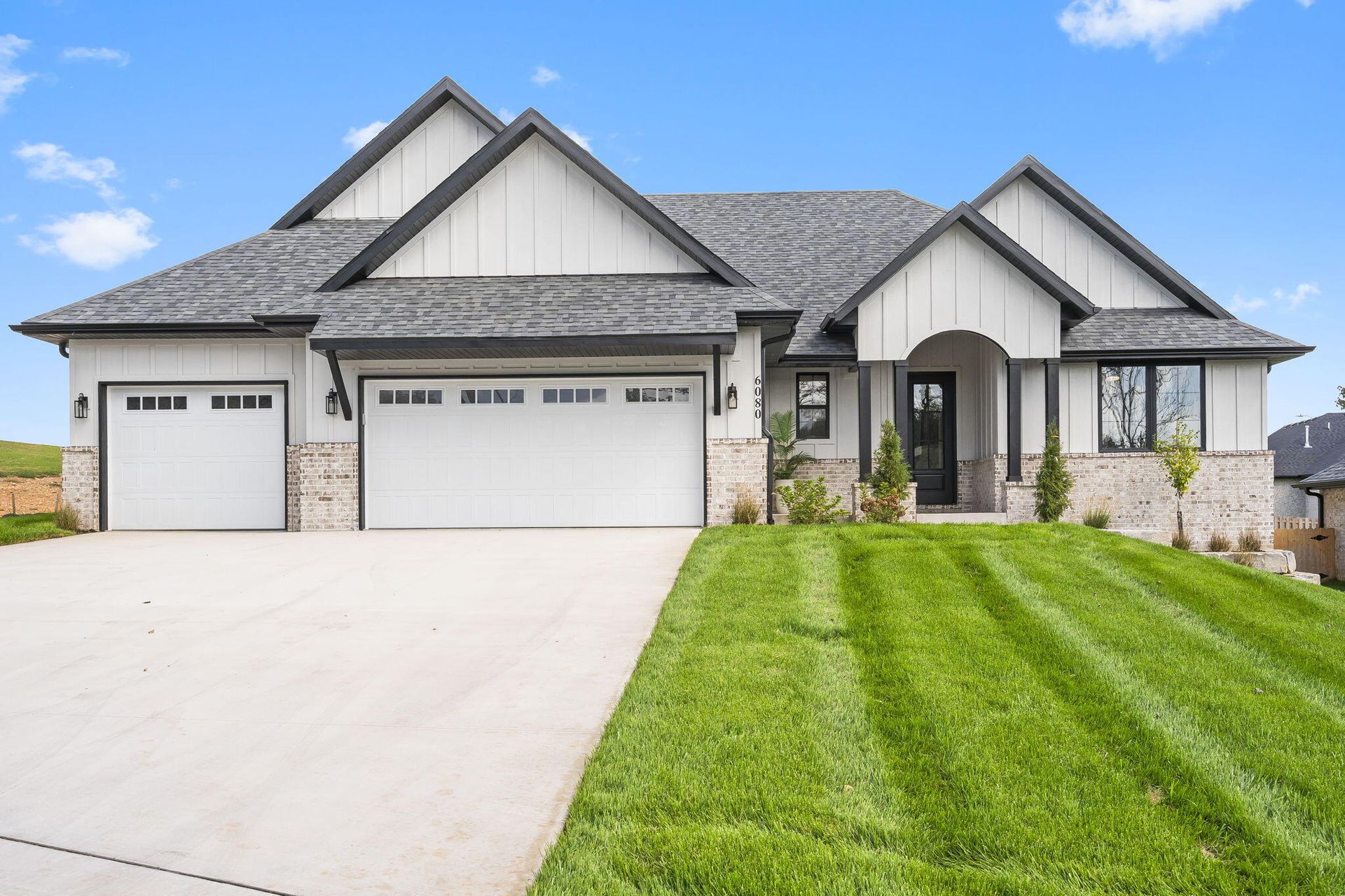 Modern white house with gray roof, brick accents, and a well-manicured lawn and driveway.