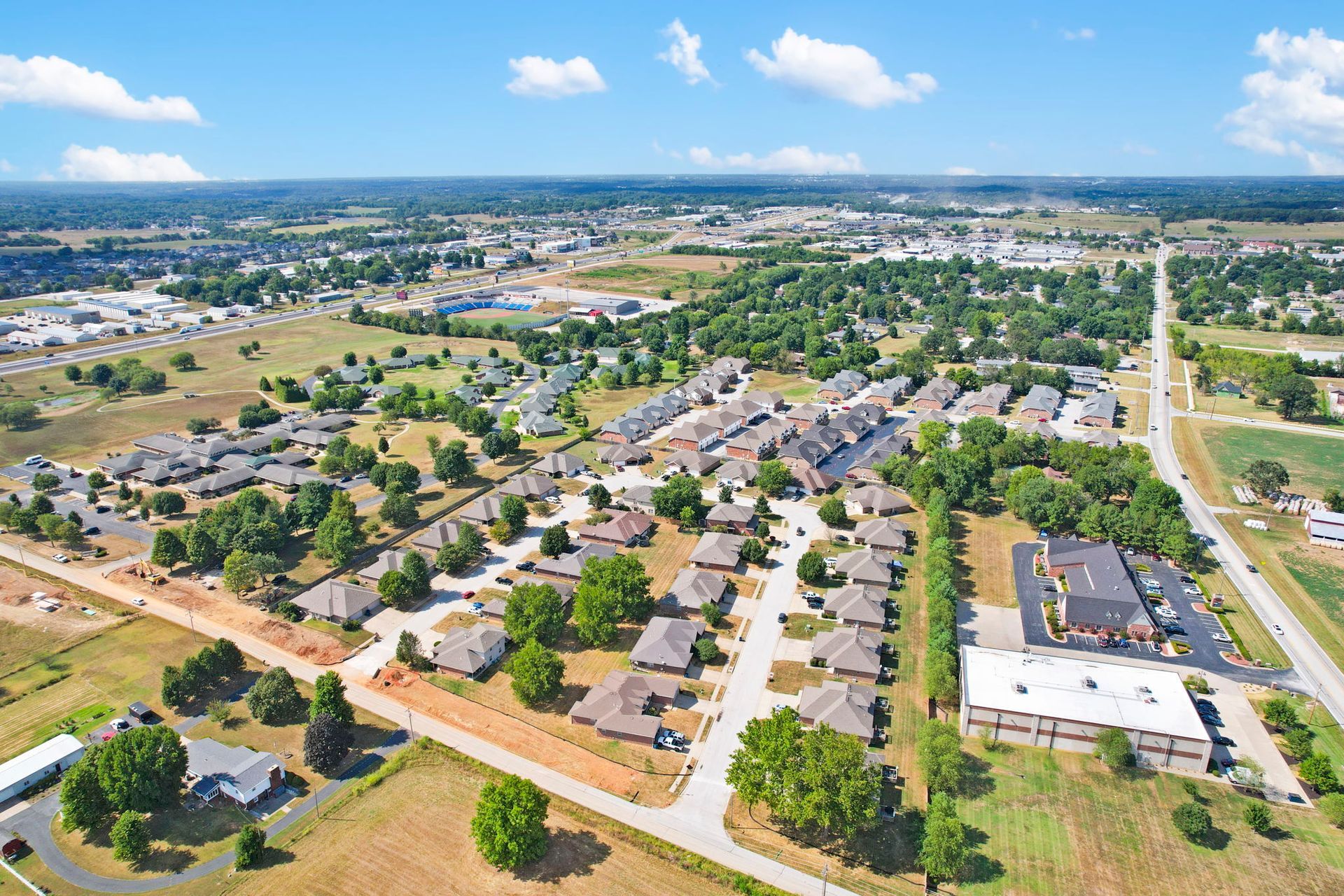 Aerial view of a suburban development with a lake, roads, and construction, bathed in golden sunlight.