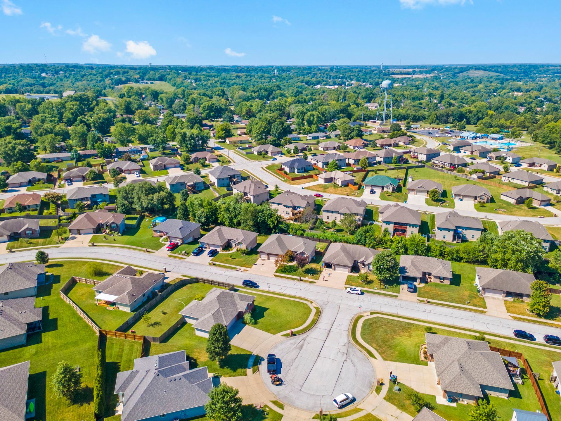 Vast green forest under a partly cloudy blue sky. Trees cover rolling hills, reaching towards the horizon.