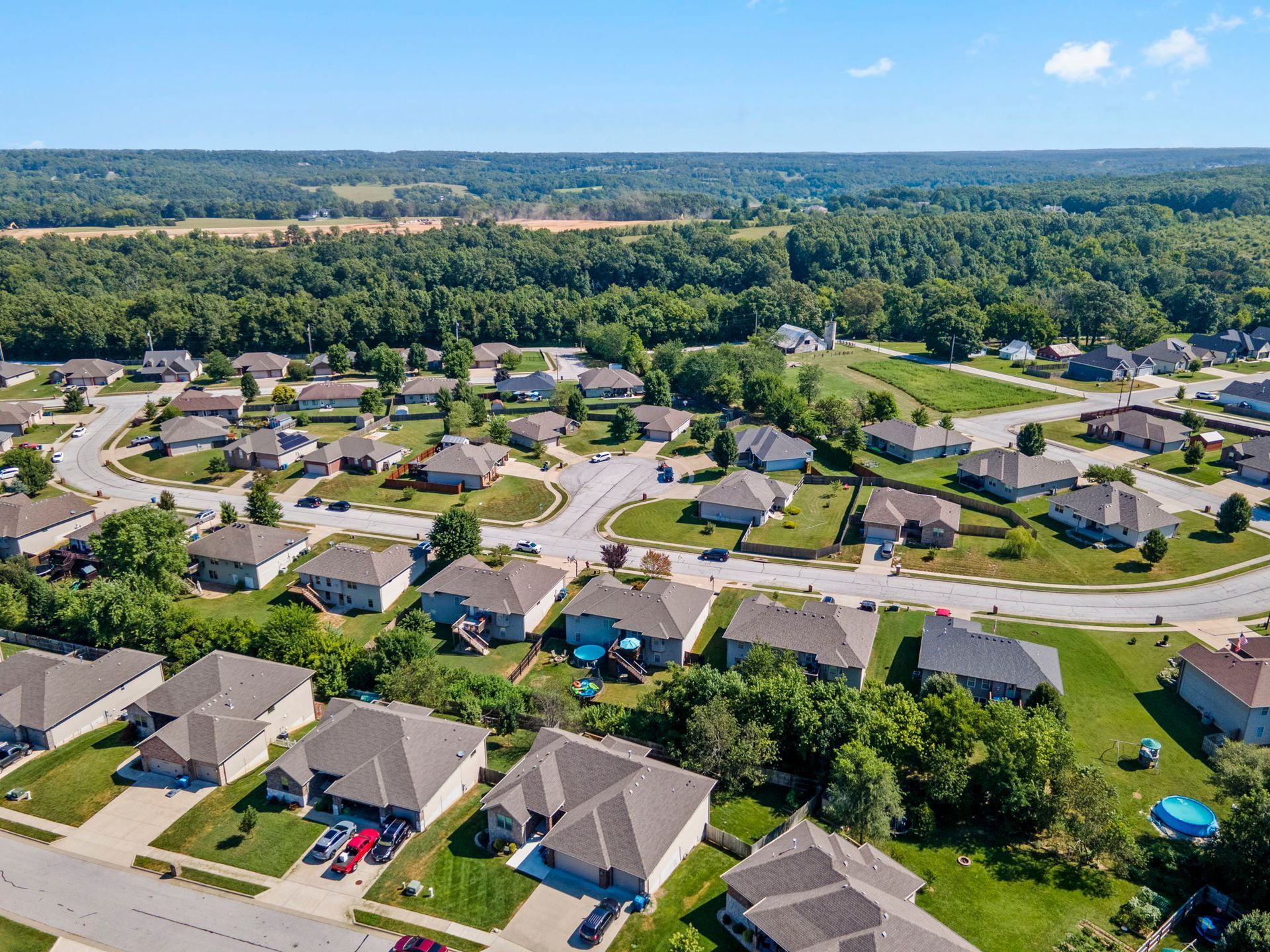Aerial view of suburban houses with green lawns and trees, under a blue sky.