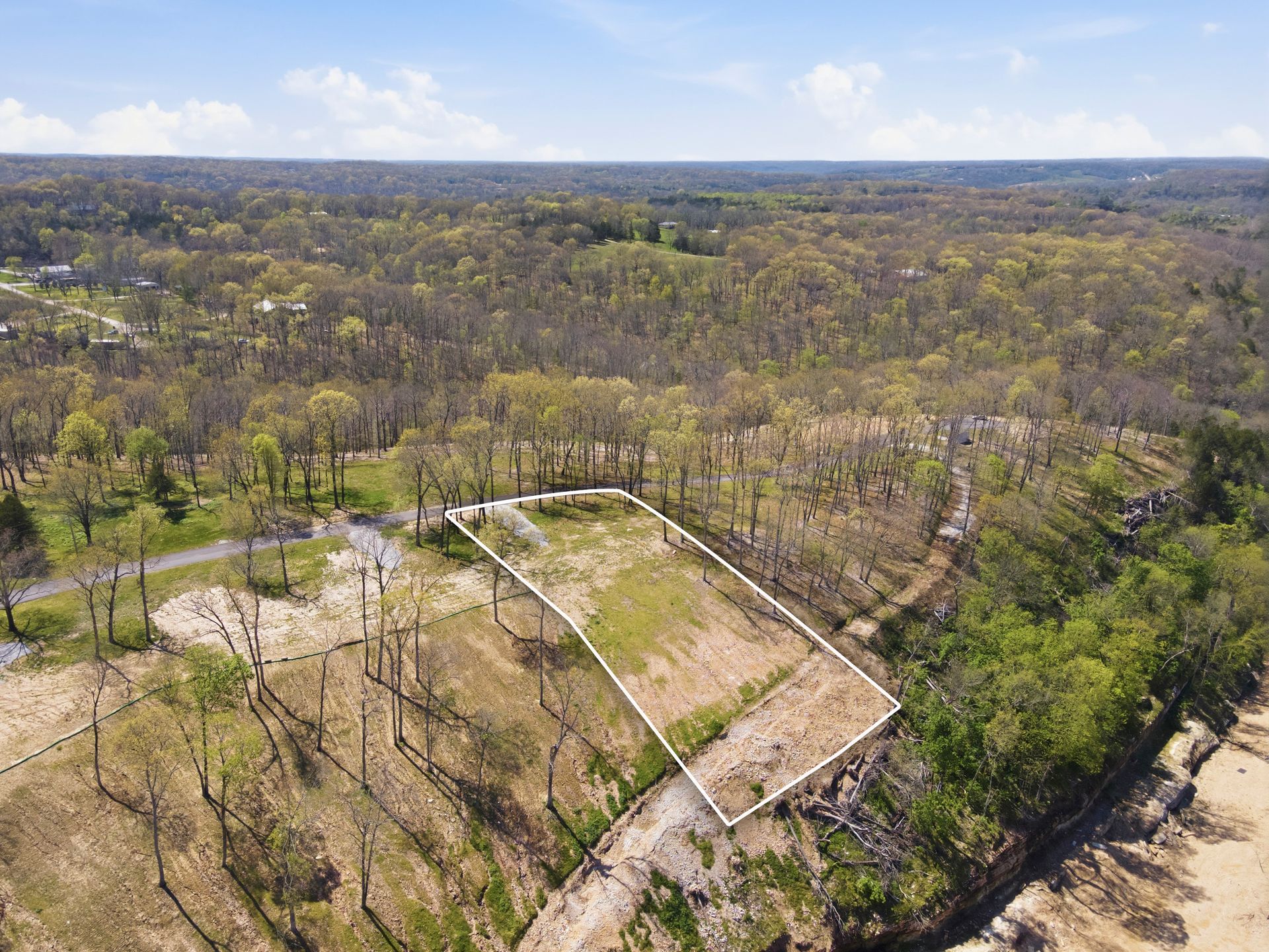 Aerial view of a wooded landscape with a cleared lot and dirt roads under a hazy sky