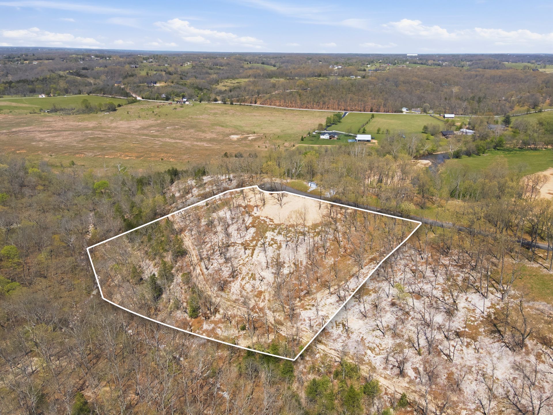 Marked rocky hillside in the foreground, with fields, trees, and a distant landscape beyond.