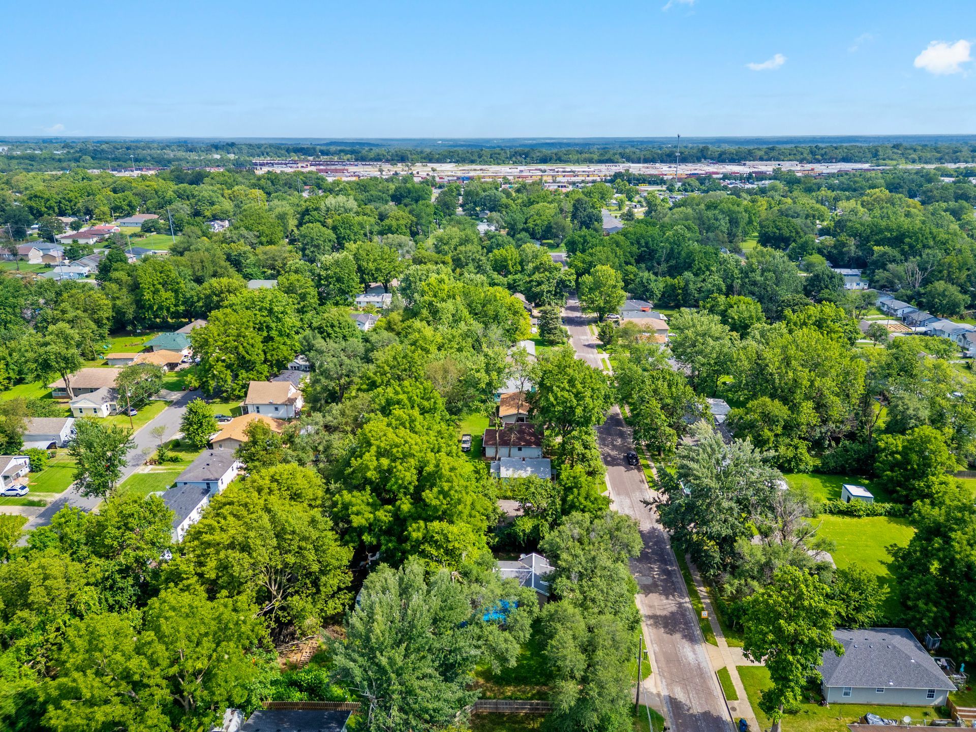 Aerial view of a row of new homes with driveways and yards, green grass, and blue sky.