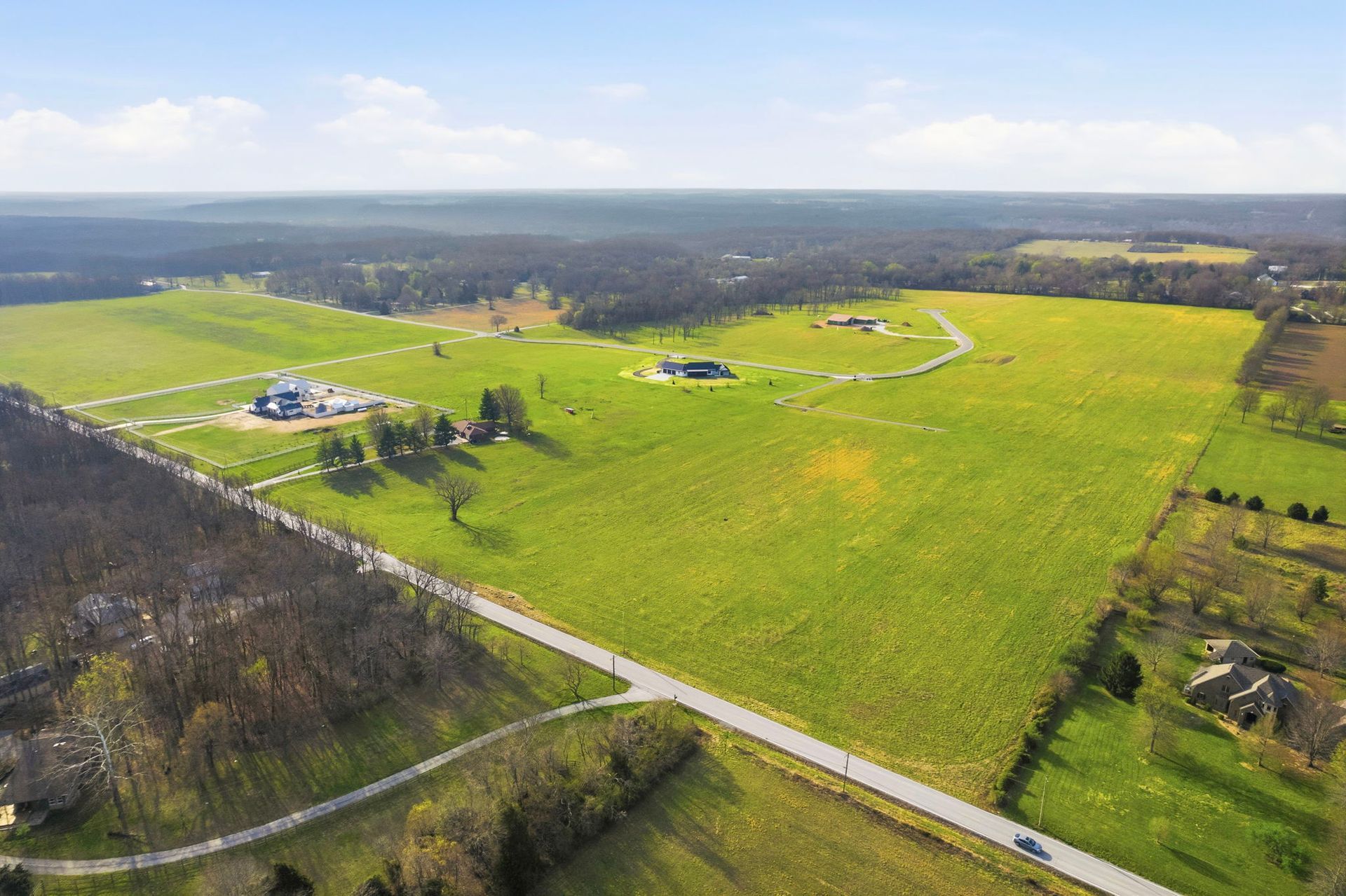 Aerial view of rural land for sale in Missouri with open fields, homes, and road near Springfield MO
