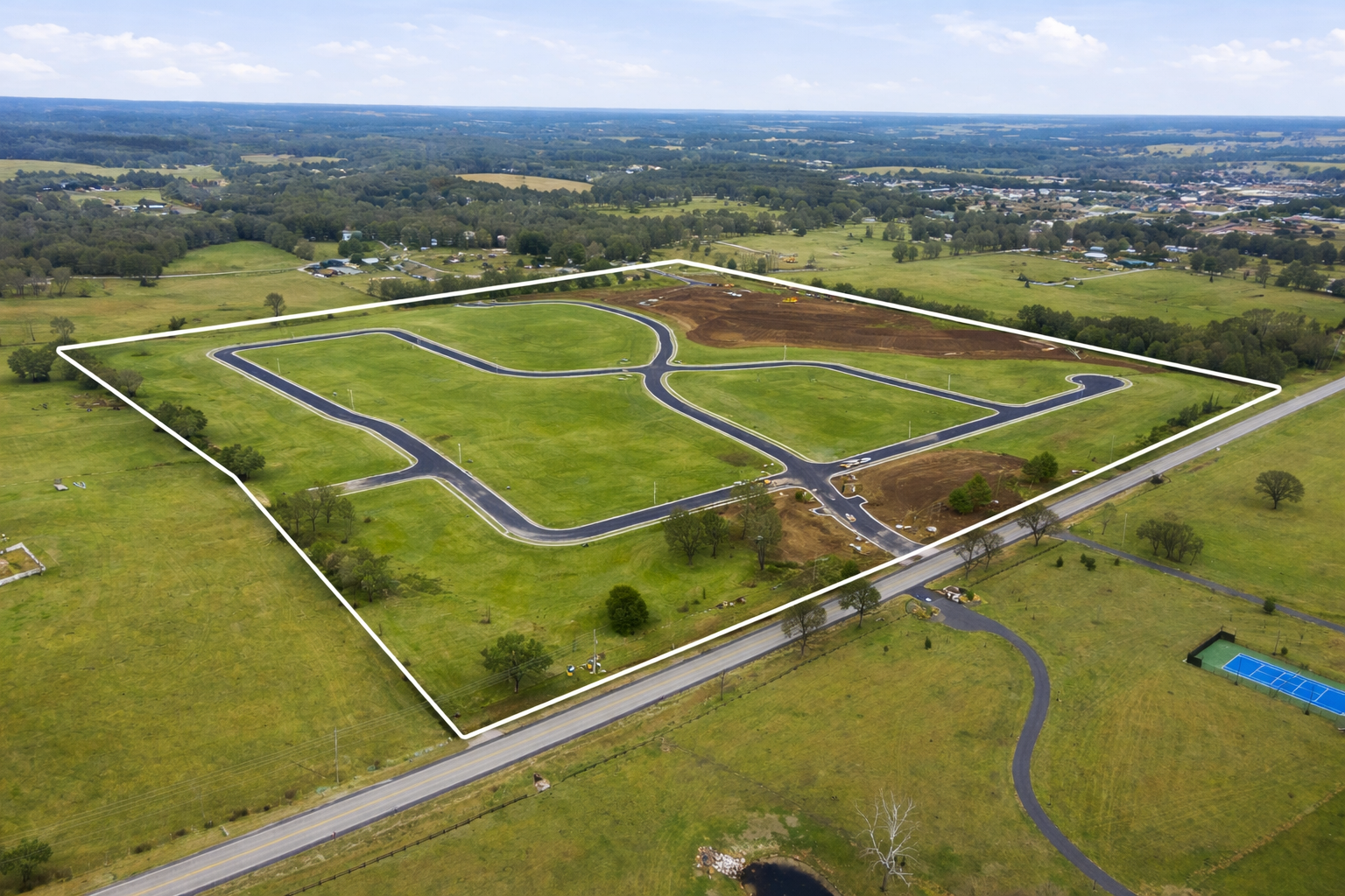 Aerial view of a community center with parking, pool, pickleball court, putting green, and surrounding trees.