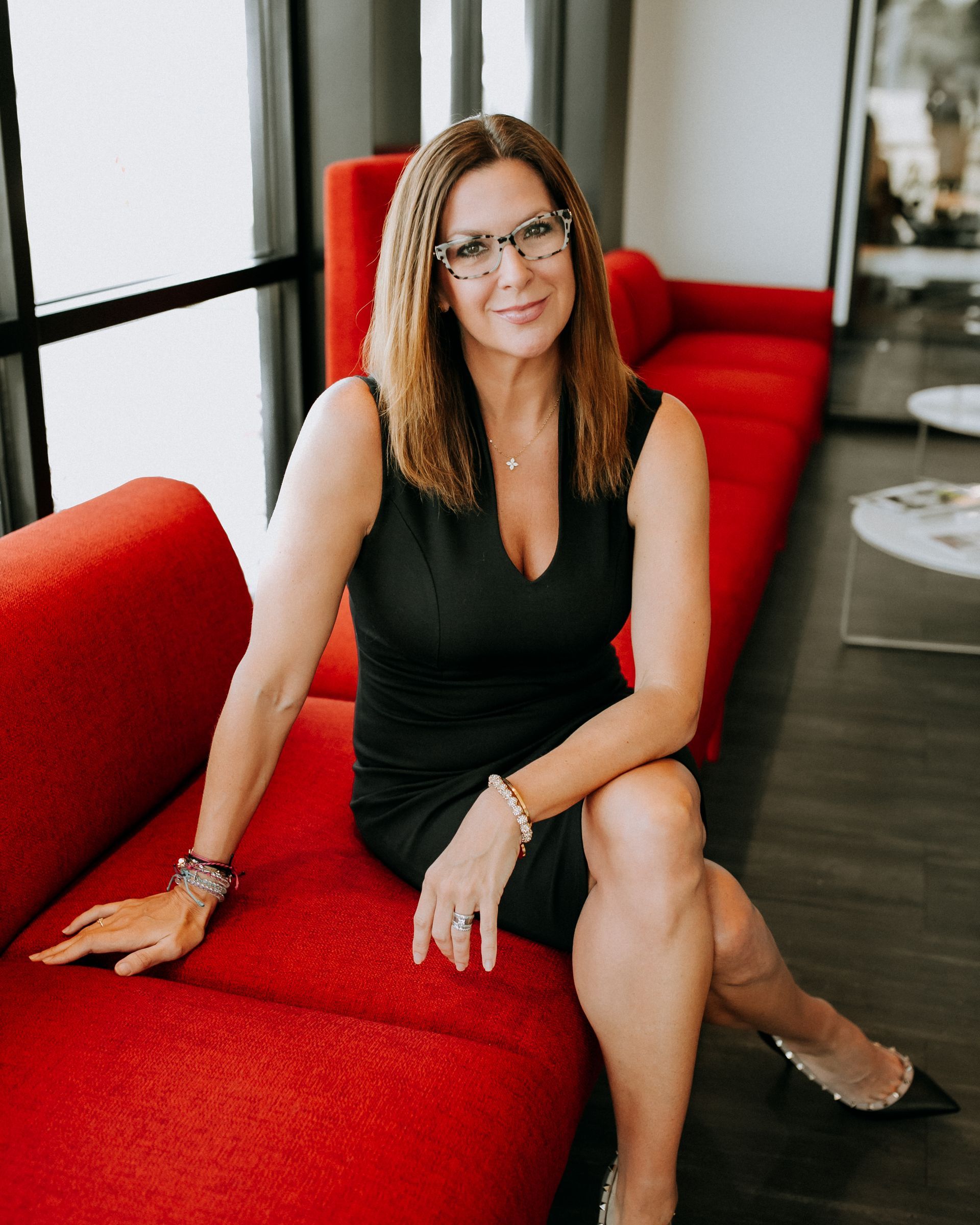 Woman in black dress sits on red couch, smiling.
