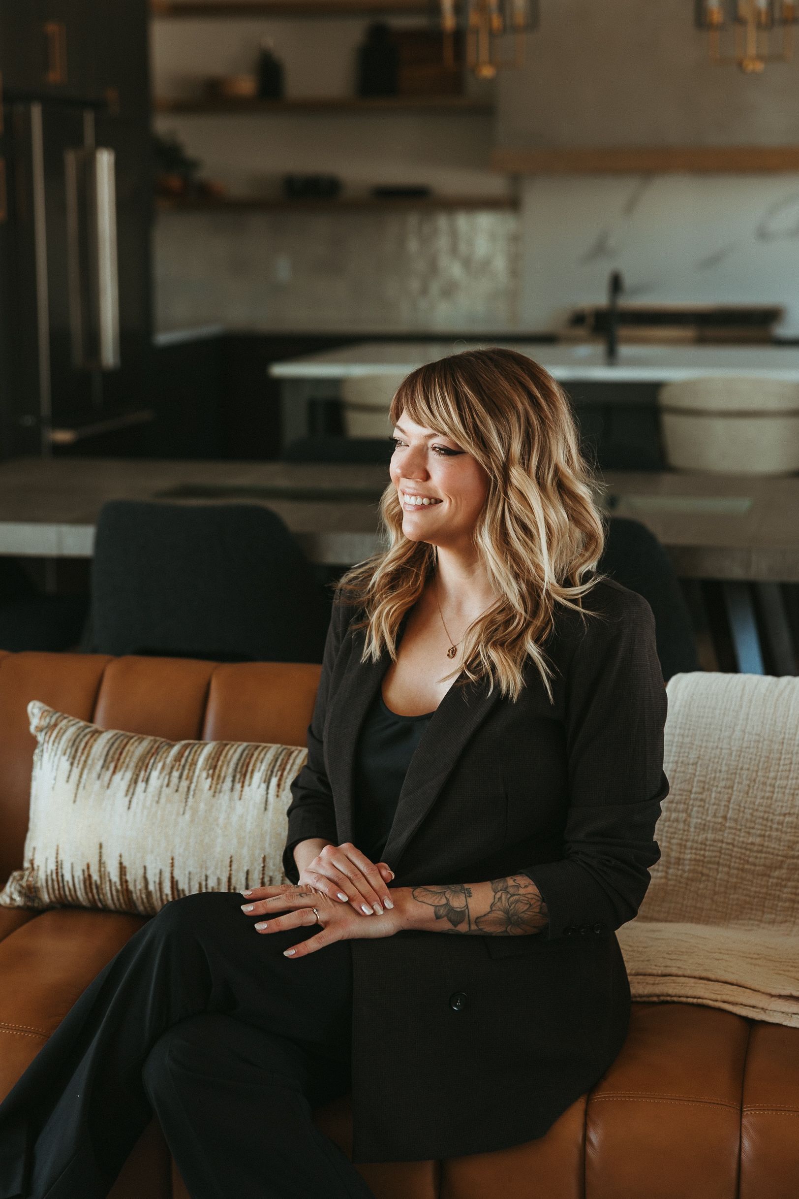 Woman with blonde hair smiling, wearing a floral dress, indoors, near a window.