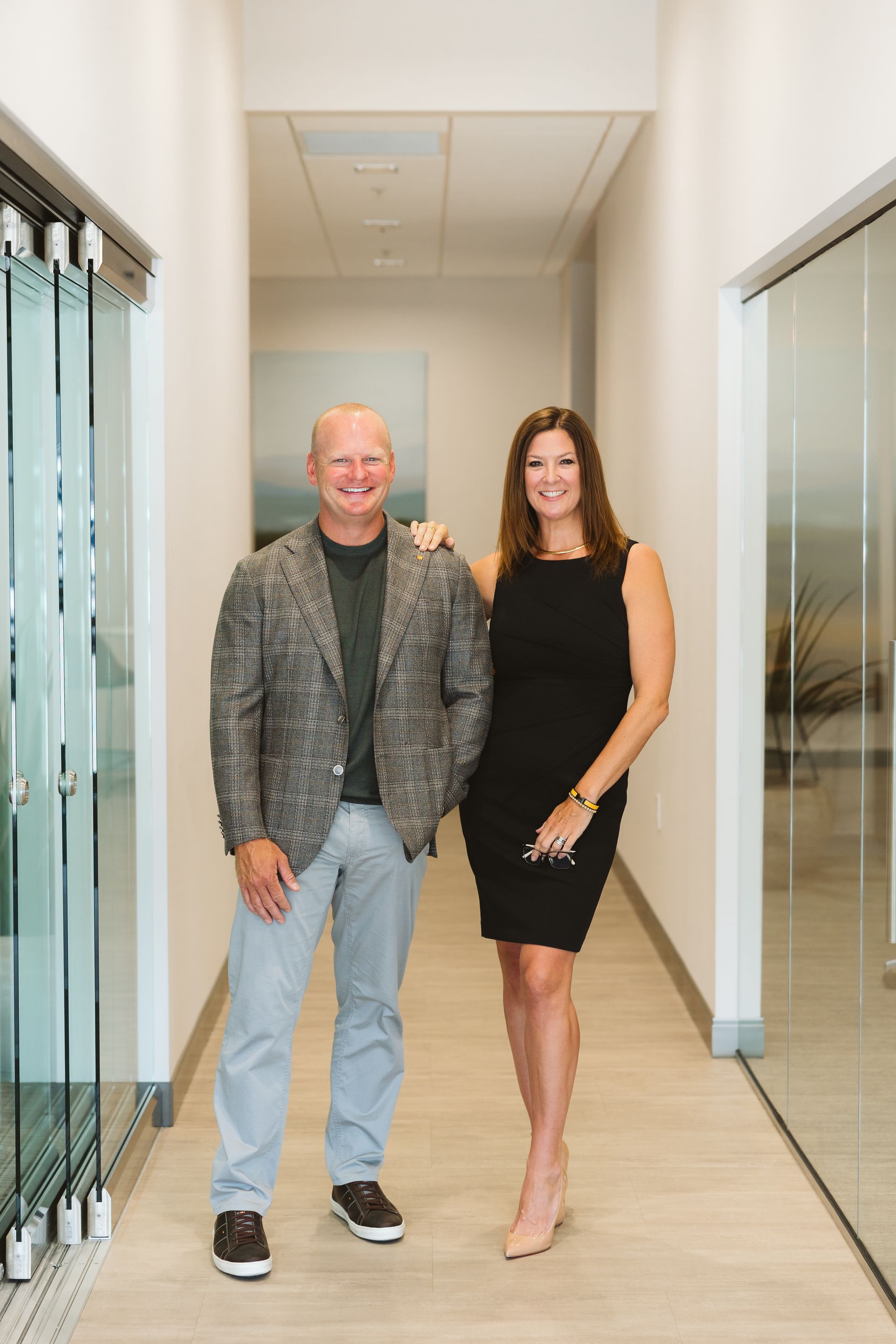 Two people in a modern living room. Man seated on a sofa, woman standing beside him, both smiling.
