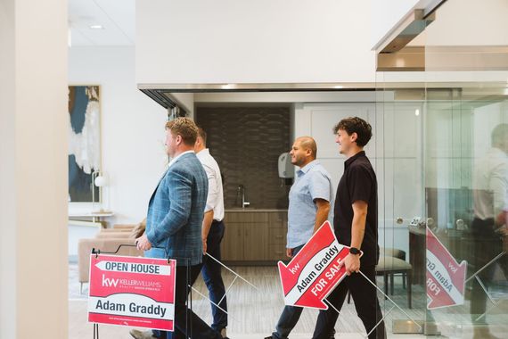 Three people walking indoors past glass walls, carrying red-and-white protest signs.