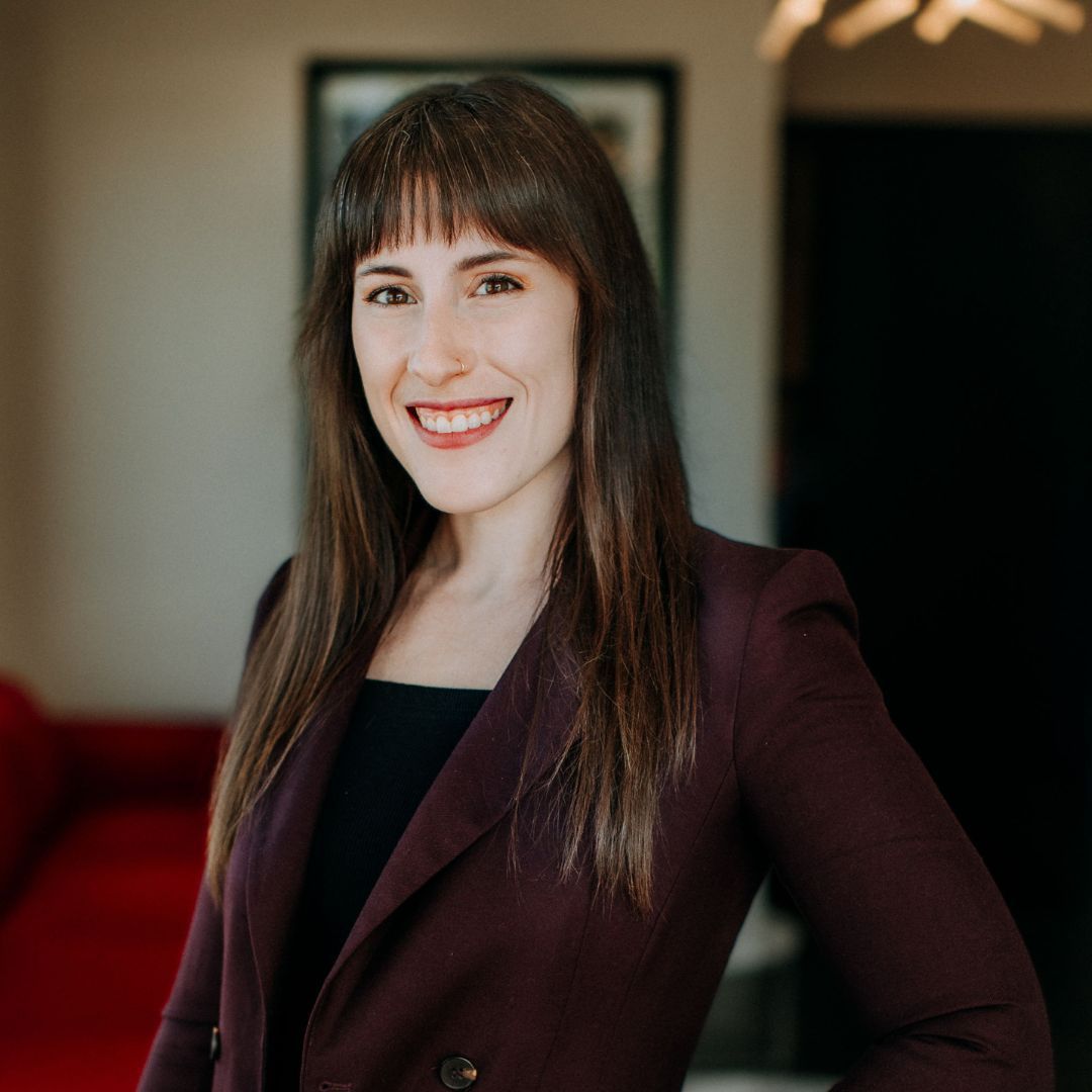 Woman with dark hair smiles, wearing a burgundy blazer and black top indoors.