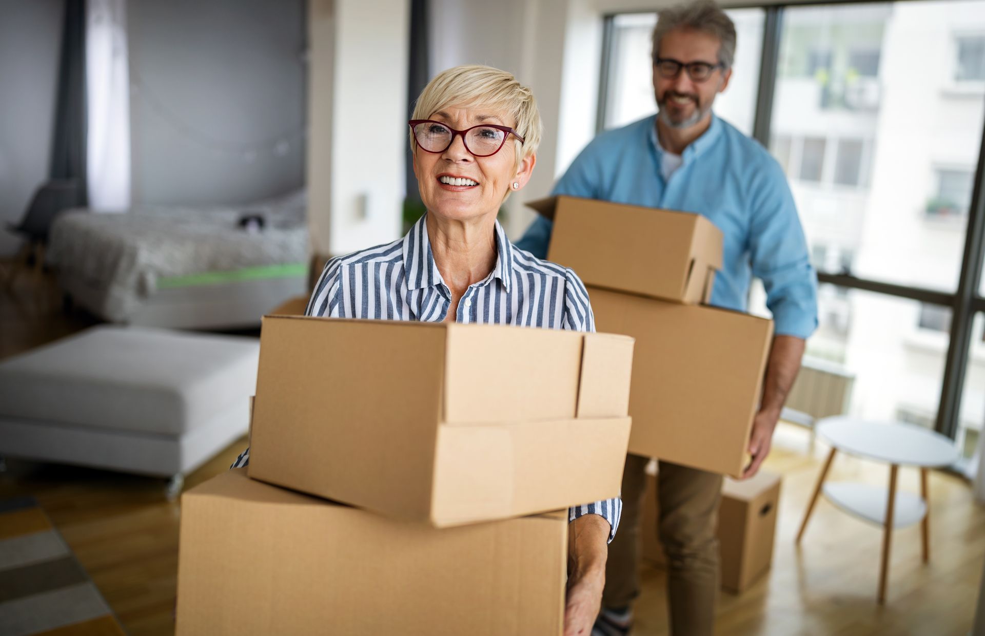 Couple carrying moving boxes while downsizing into a smaller home
