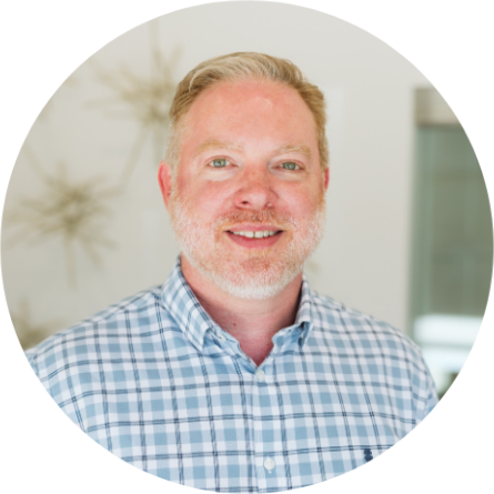 Man with fair skin and red hair smiling, wearing a blue plaid shirt.