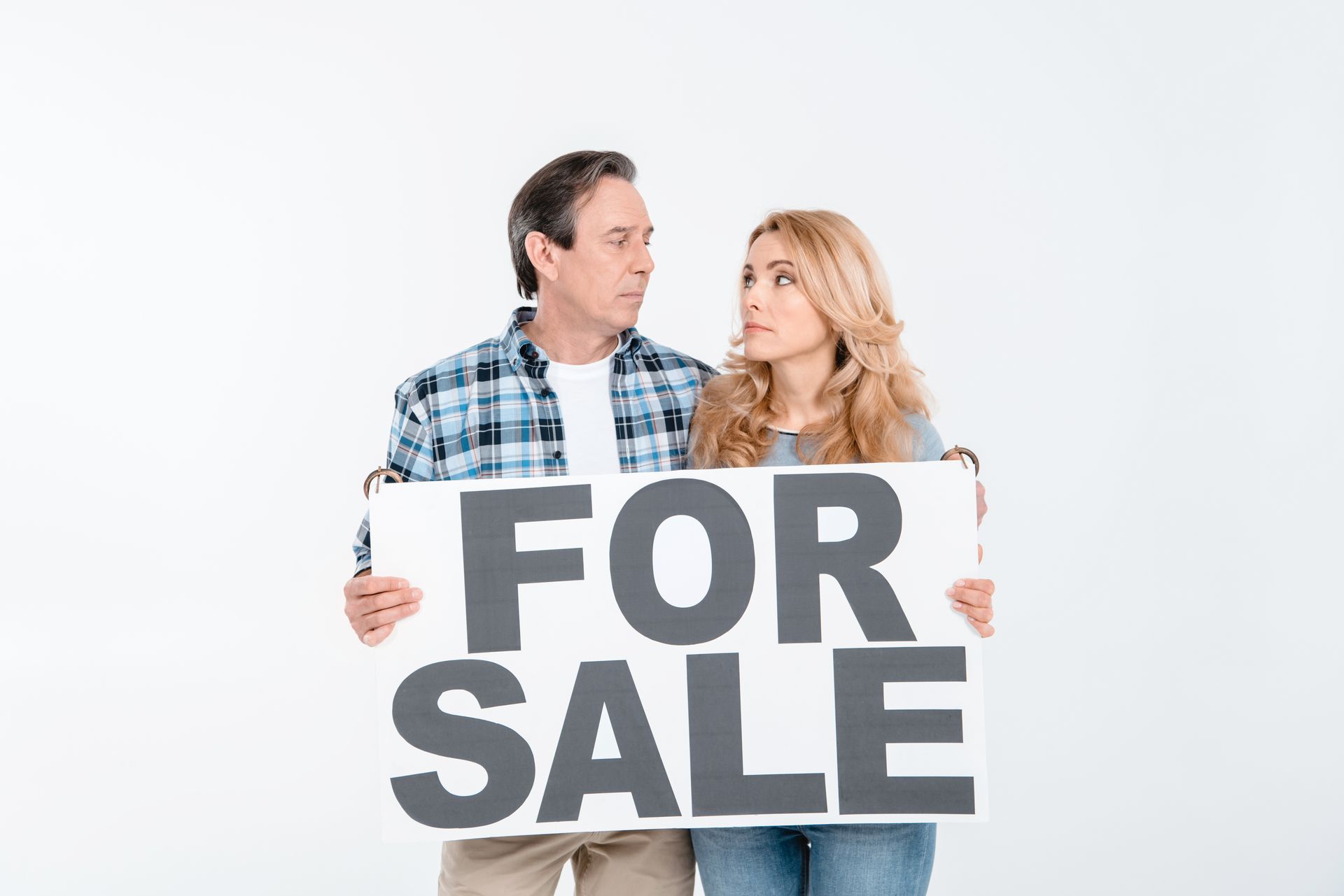Couple holding a For Sale sign while comparing FSBO and Realtor options before selling Nixa home