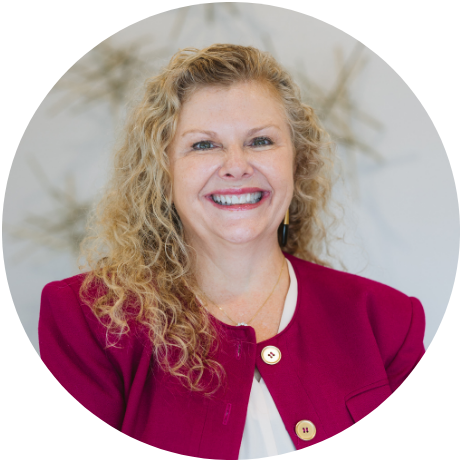 Woman with blonde curly hair smiles, wearing a red jacket and white top.