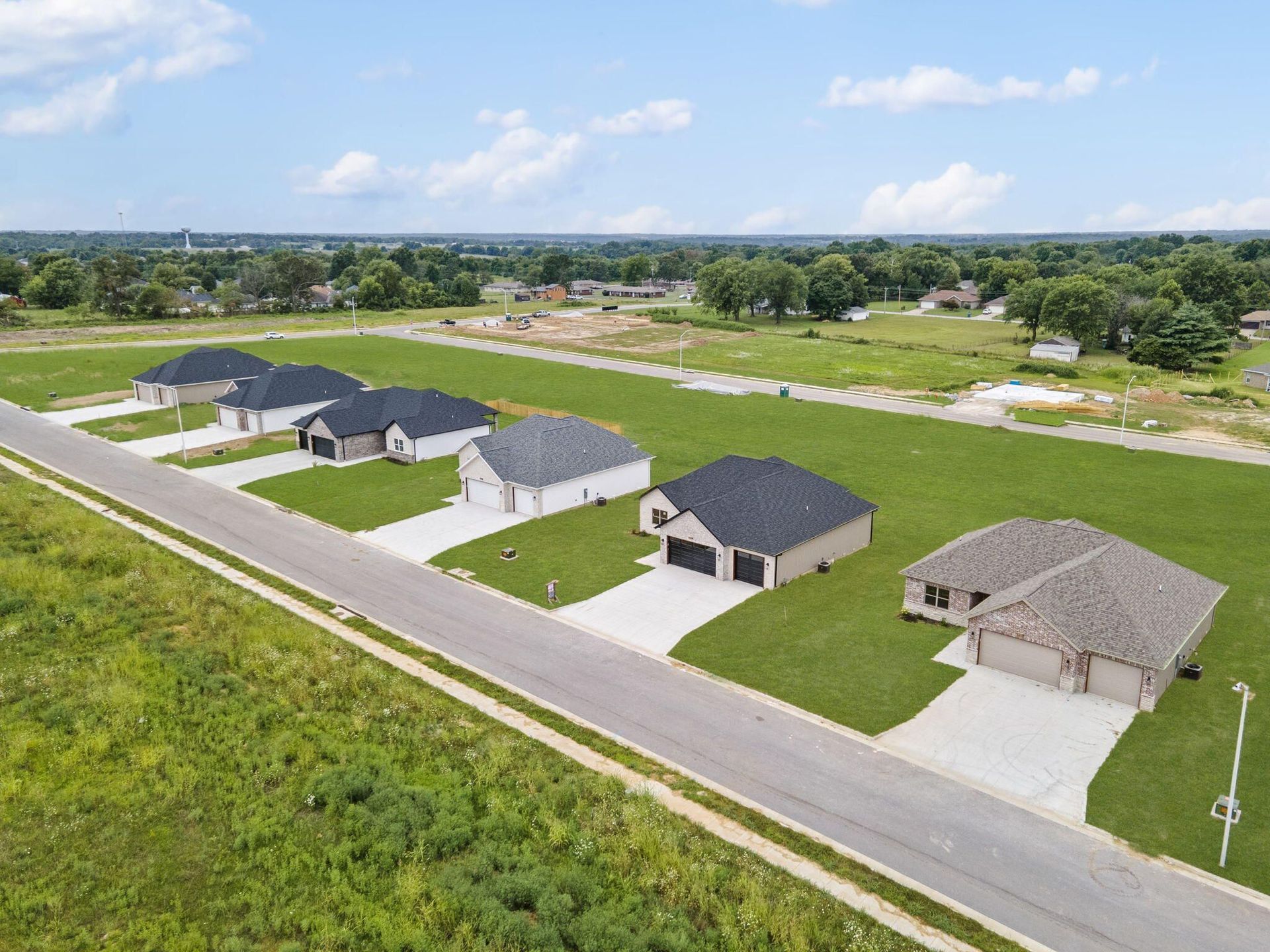 Aerial view of new houses along a street with green lawns and blue sky.