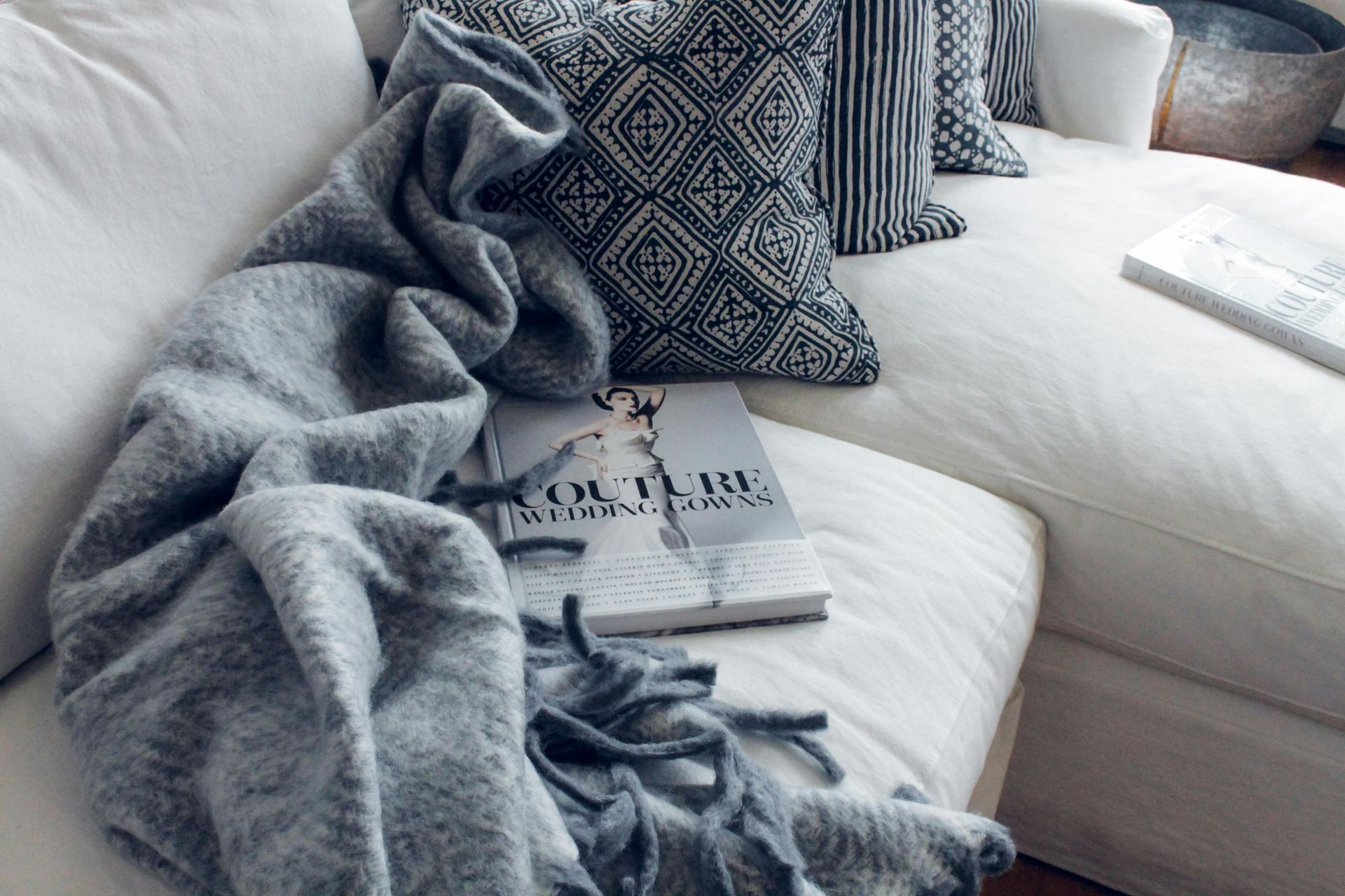 Gray blanket and book on a white couch, with patterned pillows.