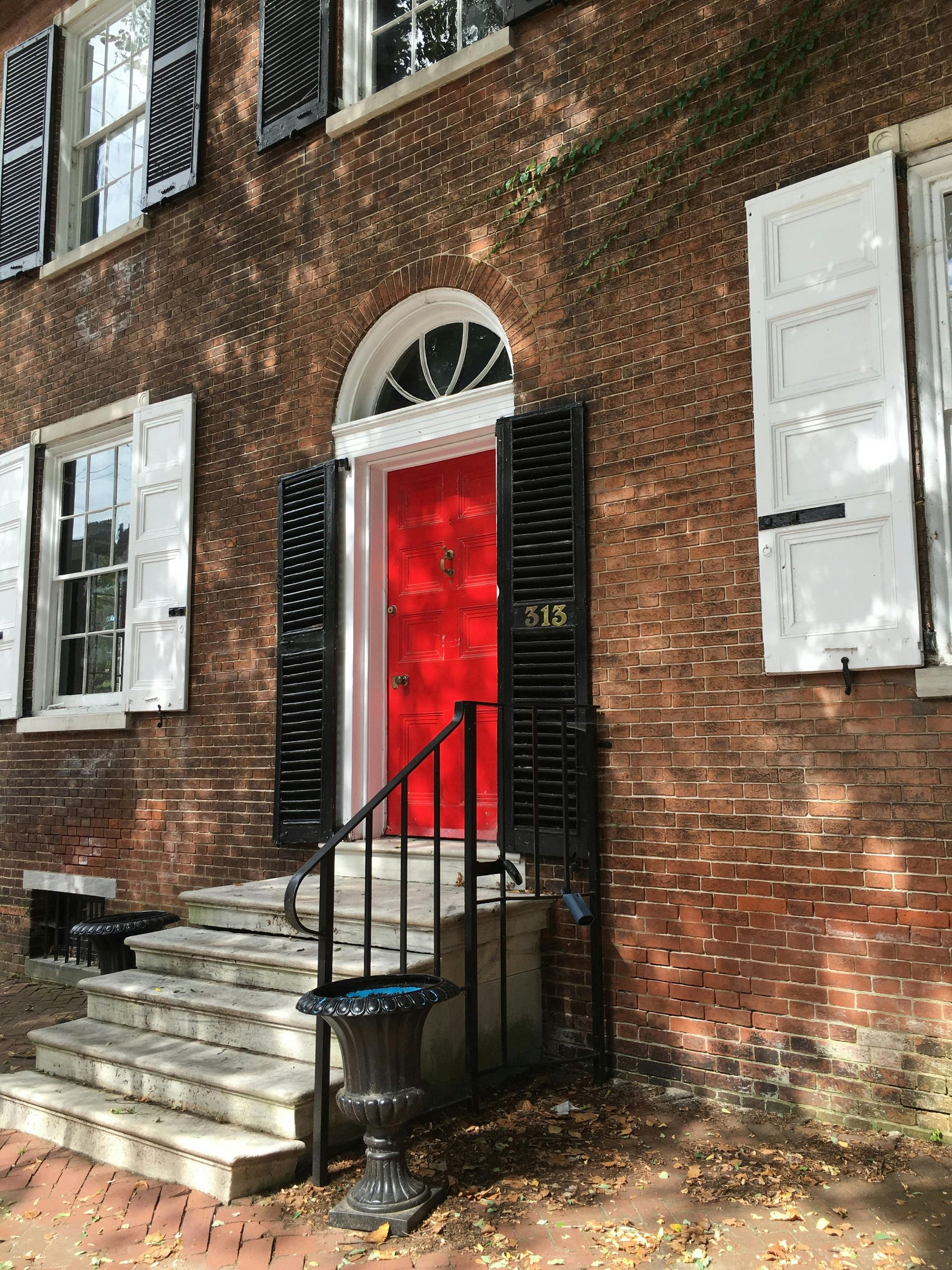 Brick building with red door, black shutters, white windows, and stone steps.