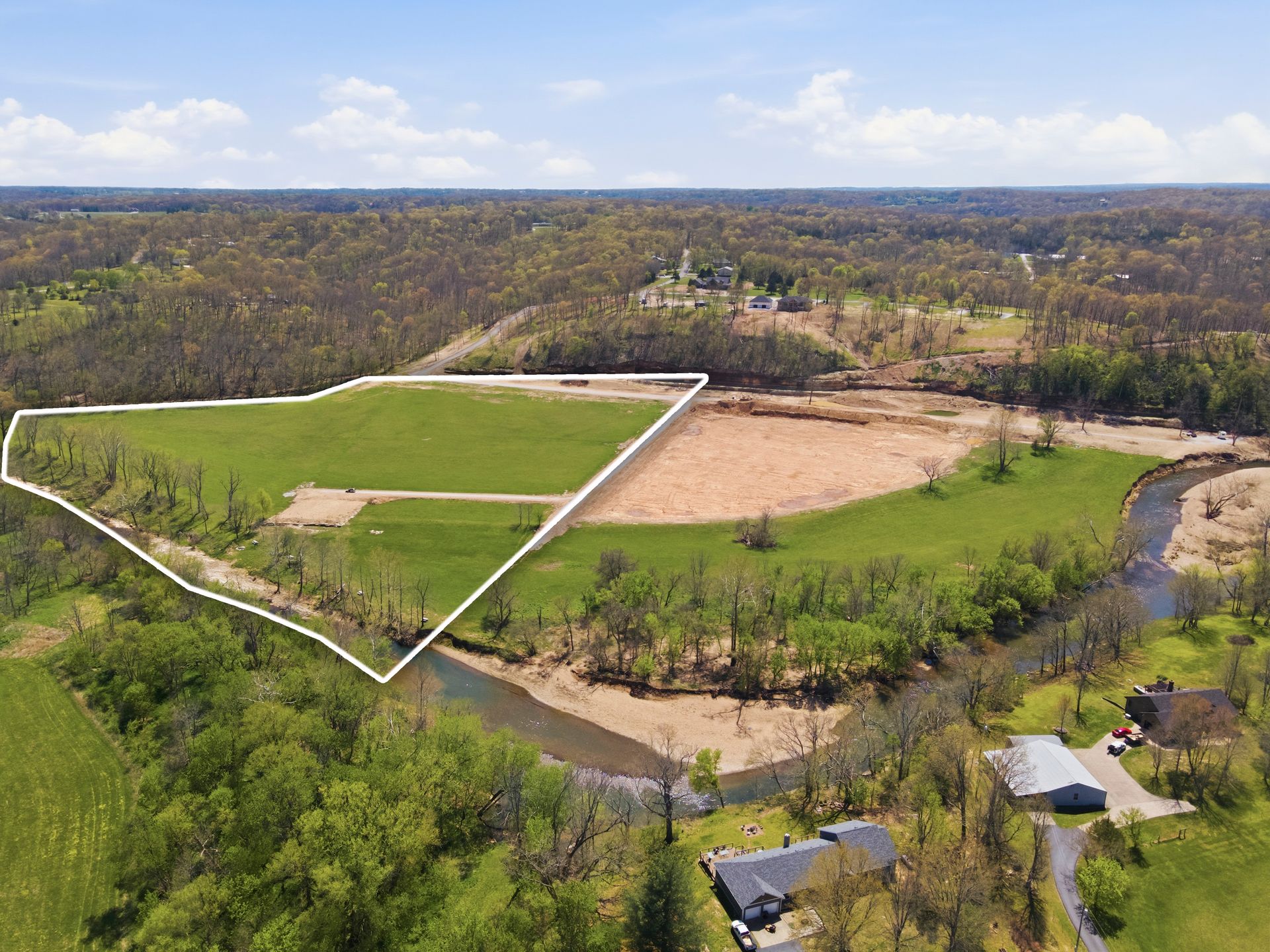 Aerial view of a rural field outlined in white, with green grass, a tan patch, and wooded hills nearby