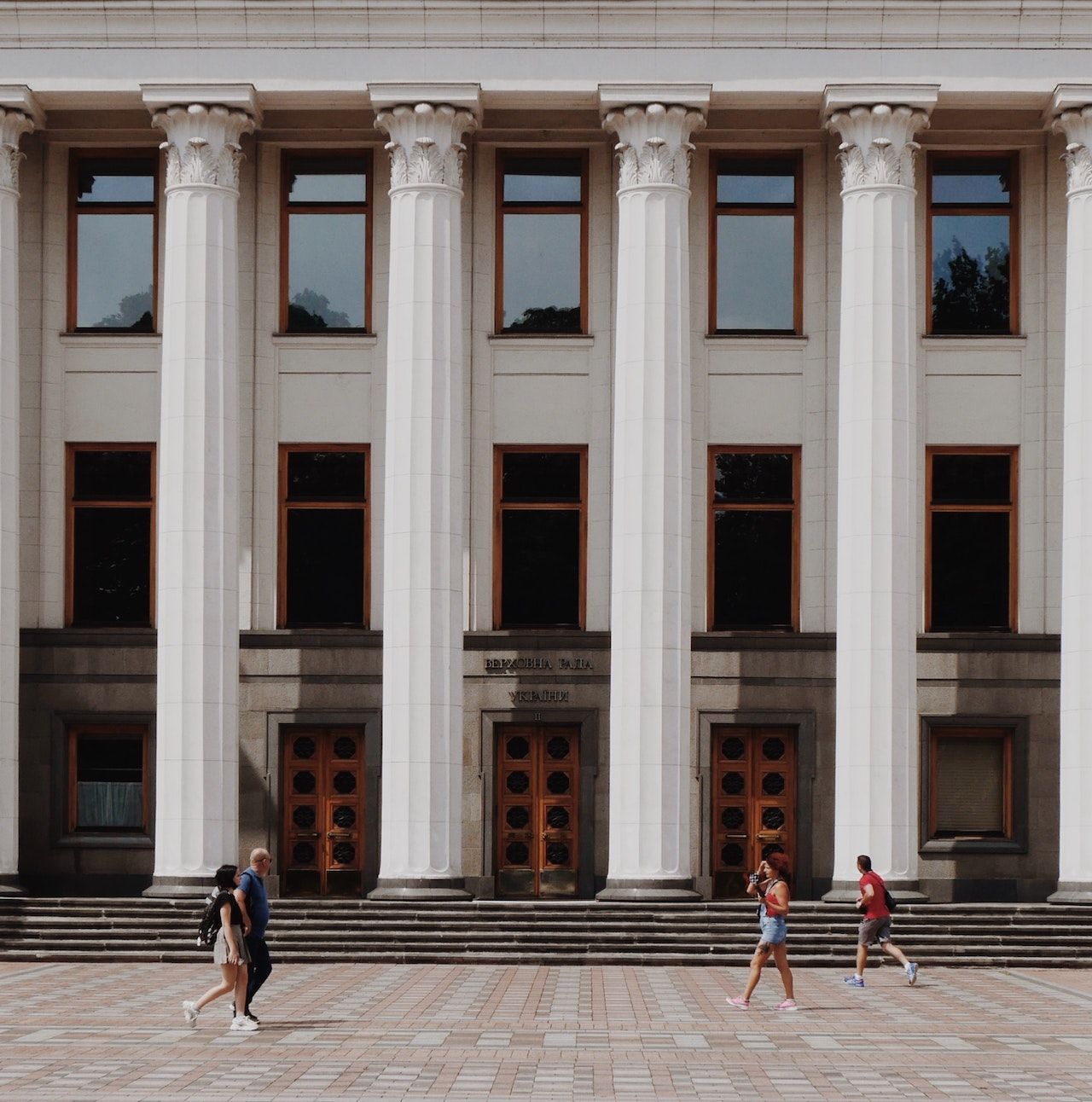 A group of people are walking in front of a large building with columns and windows.