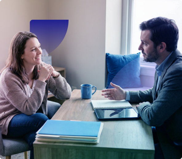 Two people talking across a table with a laptop and mug in a bright office lounge