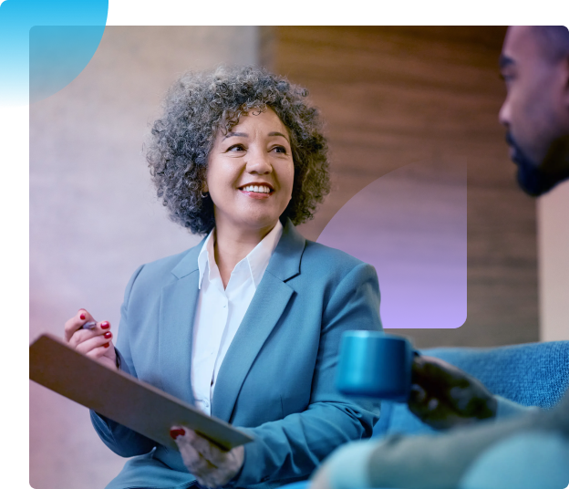 Two people talking on a couch, with one holding a folder and smiling.