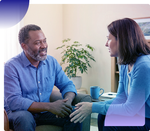 Two people talking on a couch in a bright living room, with a mug and potted plant nearby.