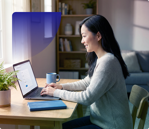 Woman working on a laptop at a table in a cozy home office, holding a blue mug.