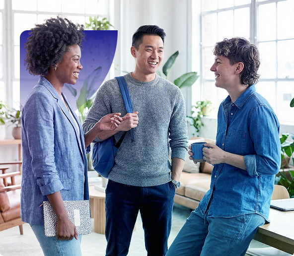 Three people chatting and smiling in a bright office lounge, one holding a cup and another wearing a backpack.