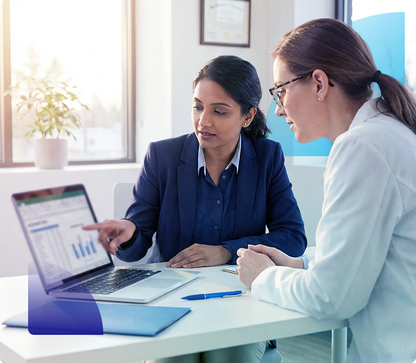 Two coworkers review a laptop chart in a bright office, discussing data at a desk.
