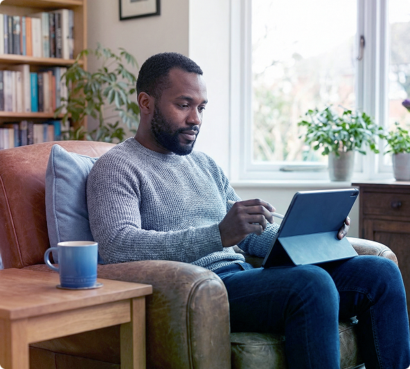 Man sitting in an armchair using a tablet beside a window in a bright living room