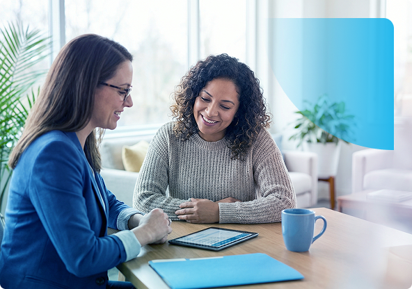 Two people meeting at a table with a tablet, notebook, and blue mug in a bright office