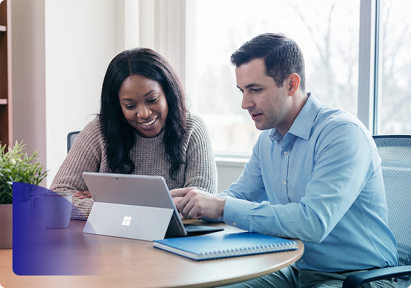 Two coworkers smiling while looking at a laptop at a table near a window