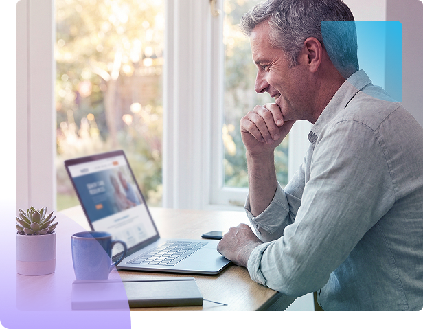 Man smiling at laptop on a bright desk with a notebook and coffee mug