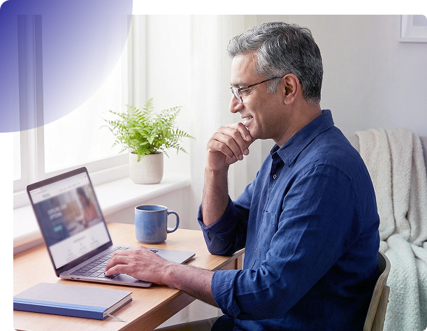 Man typing on a laptop at a desk with a mug, notebook, and plant in a bright home office