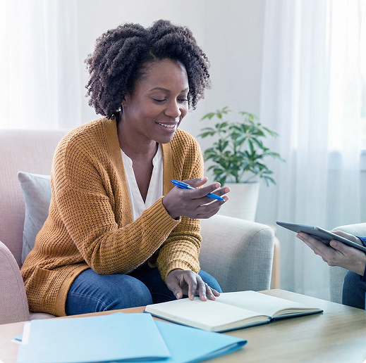 Woman smiling on a couch, using a smartphone during a meeting at a table with papers and a laptop